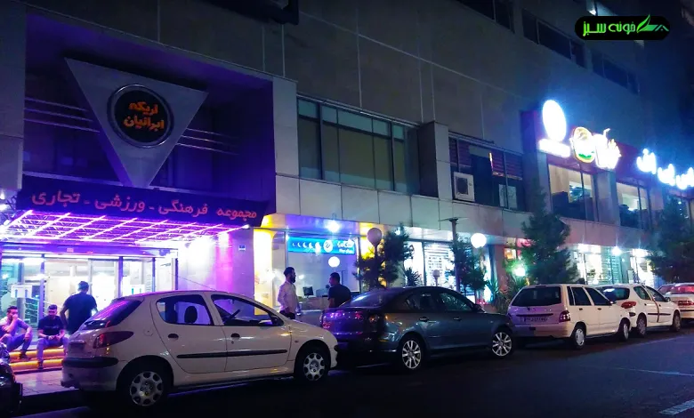 نمای بیرونی یک ساختمان در شب با تابلویی به زبان عربی که نام را نشان می‌دهد، چند ماشین پارک‌شده در مقابل و نورپردازی بنفش و آبی در ورودی.